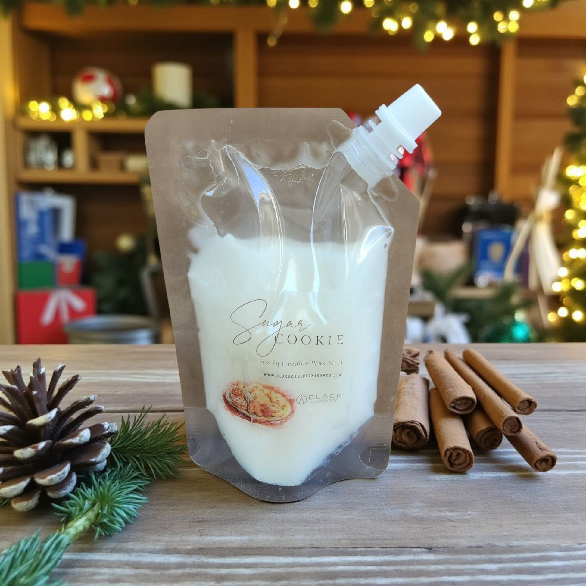 Packaged product labeled 'Sugar Cookie' with cinnamon sticks and a pine cone on a wooden surface.